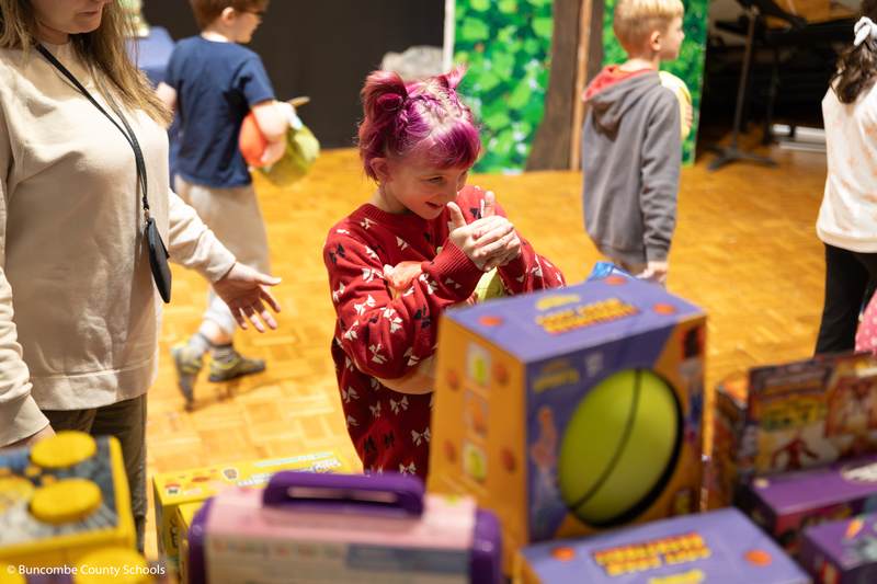 Little girl with purple hair smiling big as she is looking at all the toy options.