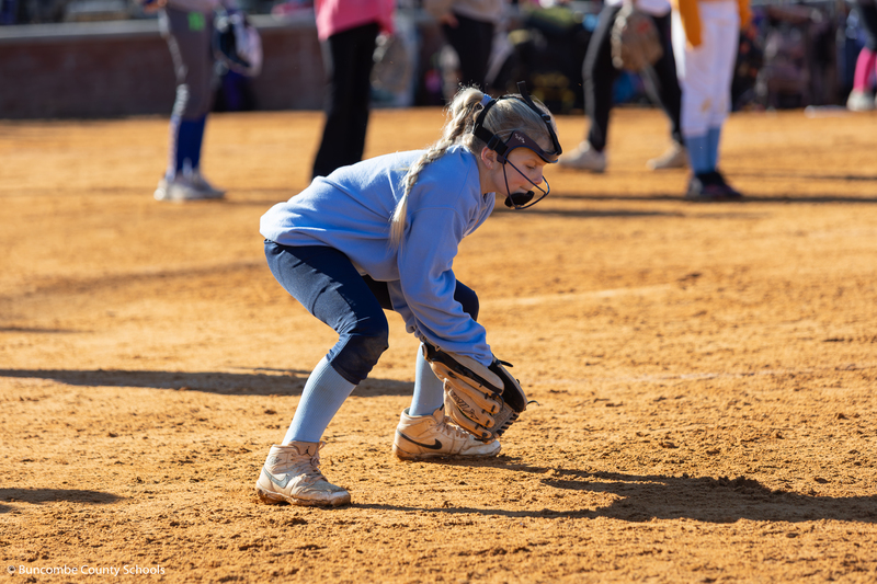 Little girl squatting down with her glove trying to catch a ball.