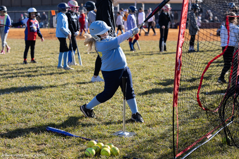 Little girl wearing blue swinging a bat, and hitting a ball of a tee.