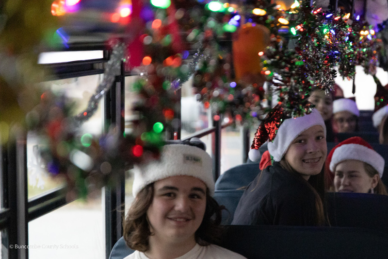 close-up of students in Santa hats and holiday decorations above them on the bus.