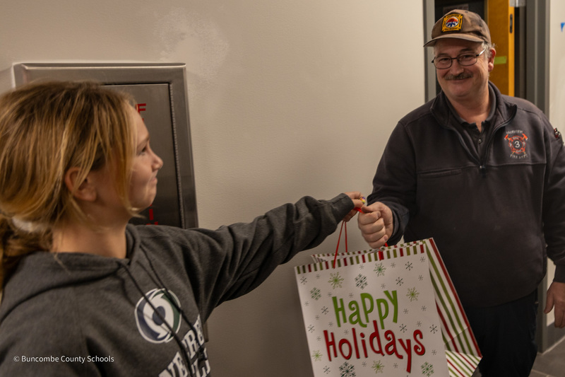 A student hands a firefighter a gift bad that says "Happy Holidays"