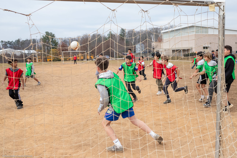 Students in red and green vests play soccer.