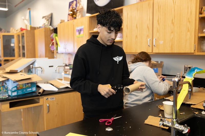 Male student cutting a paper towel cardboard insert. 