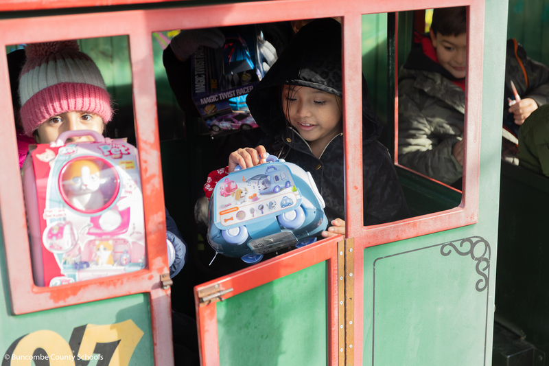 Two little girls sitting in a miniature train looking at their toys they just received.