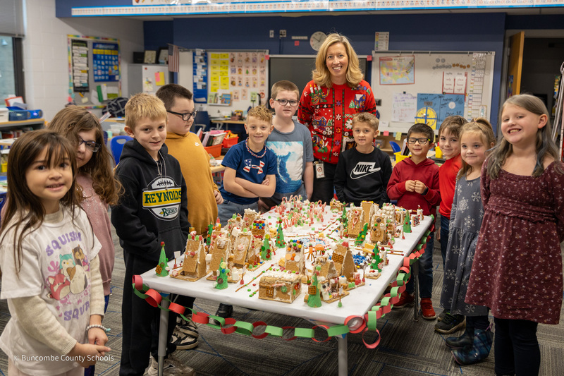 Mrs. Cheatham and her students stand around a table filled with gingbread houses created by students