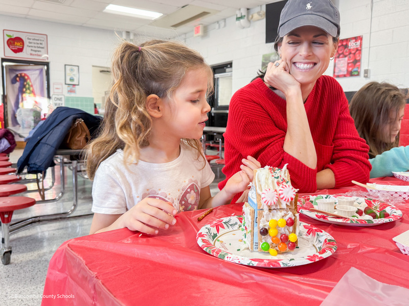 student deorates gingerbread house as parent smiles