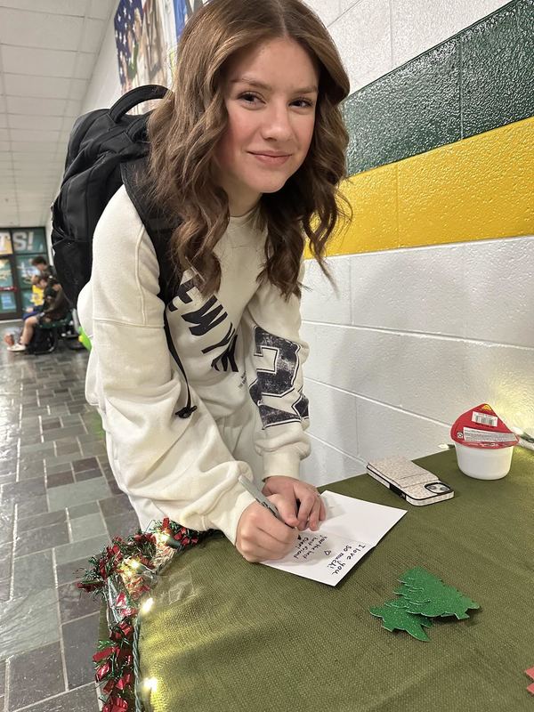 Female student smiling at the camera and writing on her holiday card. 