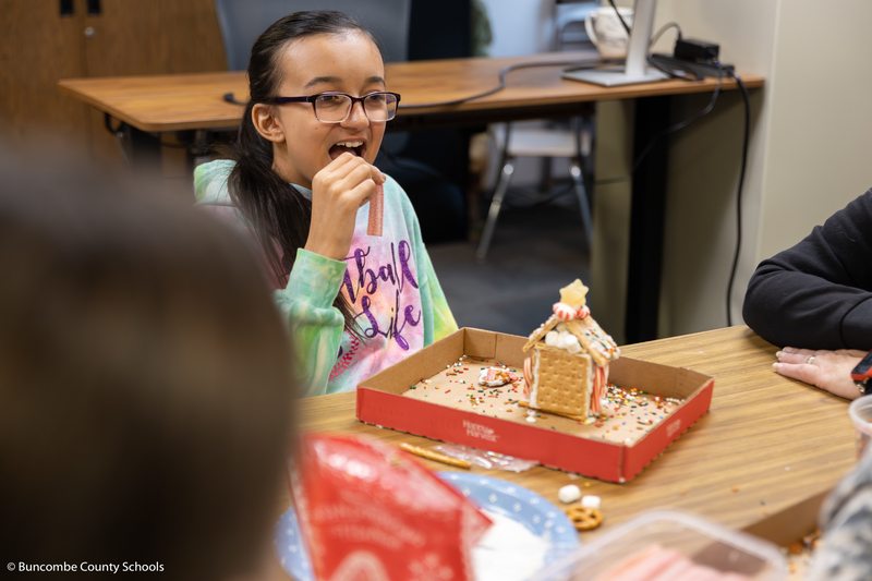 A girl in a tie dye hoodie eating a piece of candy.