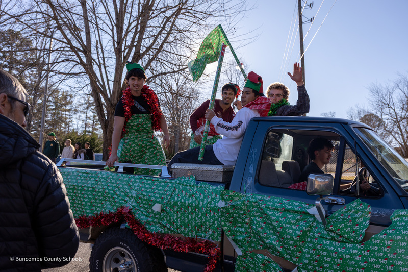 Students holding flags made of wrapping paper waves from the back of a pickup truck