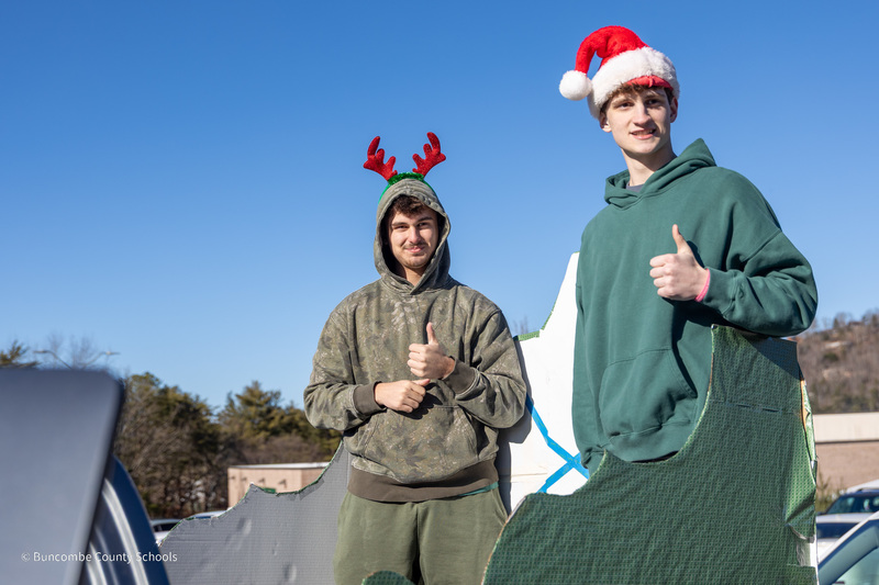 A student in a Santa hat and a student wearing reindeer antlers pose for a photo in the back of a pickup