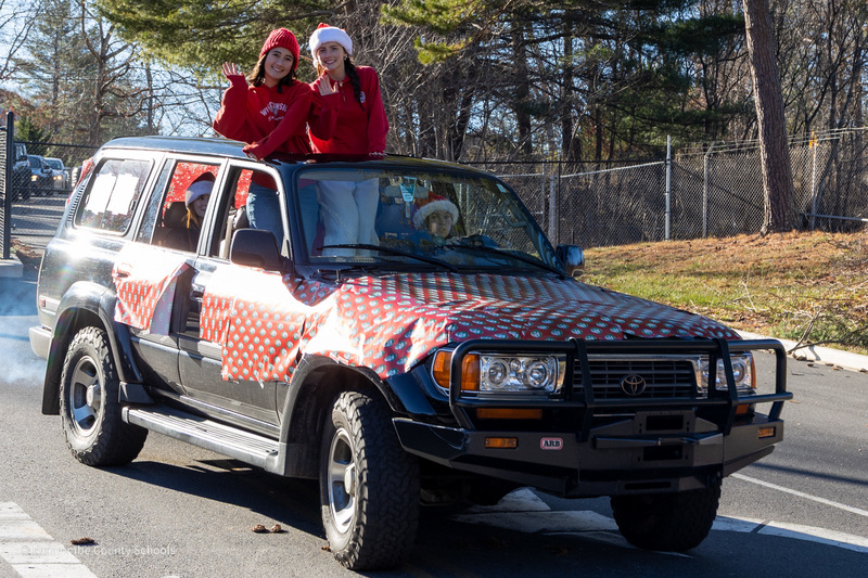 Students waving from the sunroof of a truck as it drives along the parade route