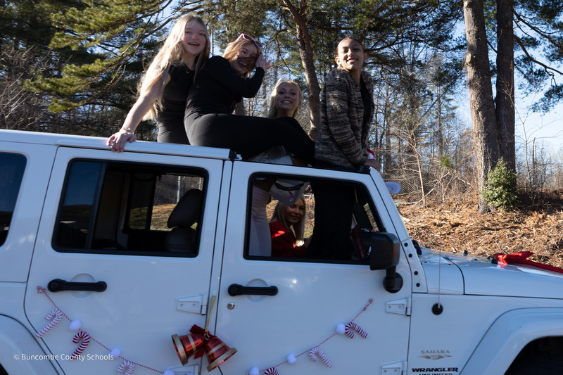 Three girls pop out of the top of a jeep and smile 
