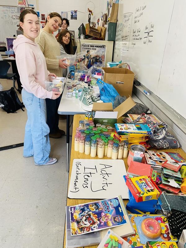 Photo of four students in front of tables lined with goodies as they assemble boxes for children in need. 
