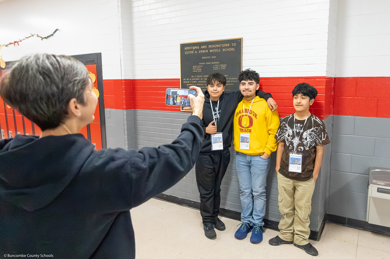A teacher takes a photo of three students.