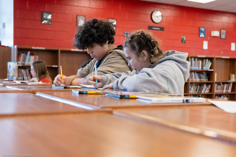 Two students write on worksheets.