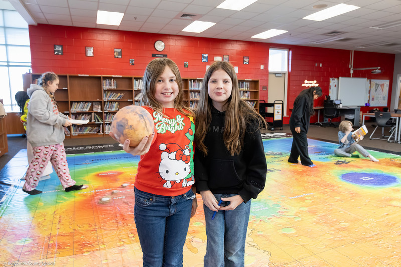 Two students pose while one holds a model of Mars.