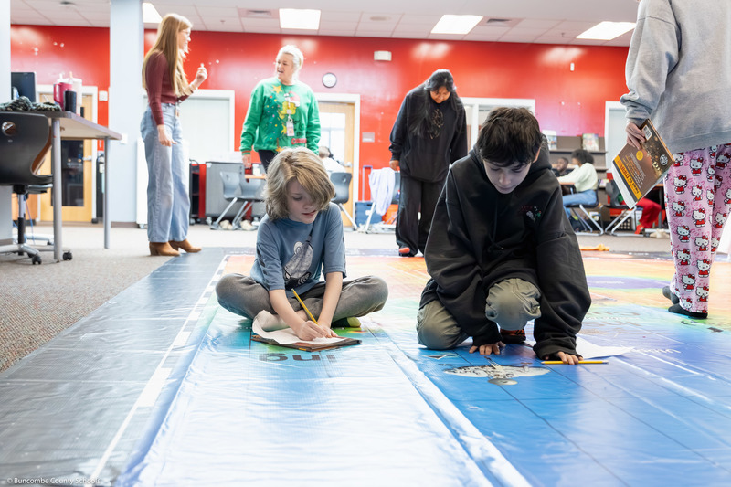 Two students write on work sheets while on the Giant Mars Map.