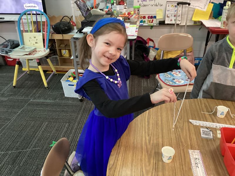 Little girl in blue dress smiling at the camera and holding up her piece of ice.