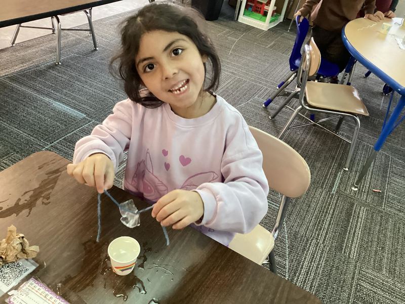 Little girl in pink sweatshirt holding up a piece of ice and smiling at the camera.