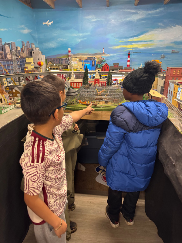 Three male students pointing at a model train. 