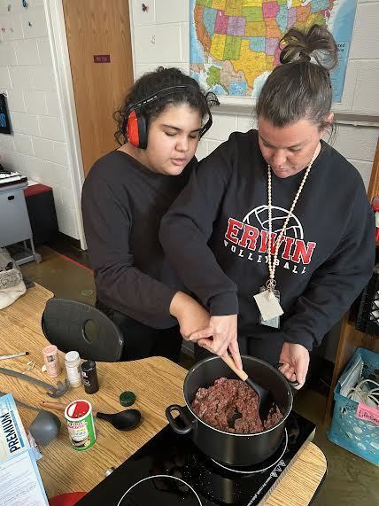 Student and teacher stirring a pot of chili together.