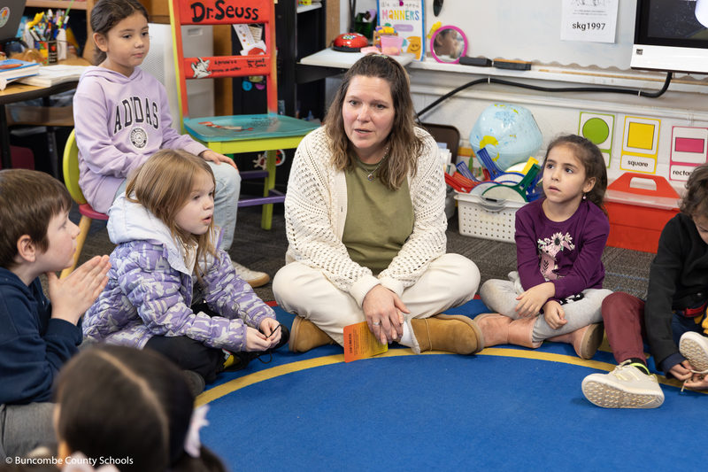 Ms. Mowery sitting in the floor with a group of kindergarteners. She telling the kids about a new breathing exercise they will be doing. 