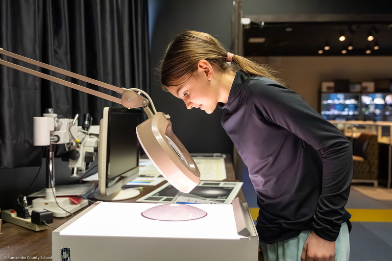 A student looks through a large magnifying glass.