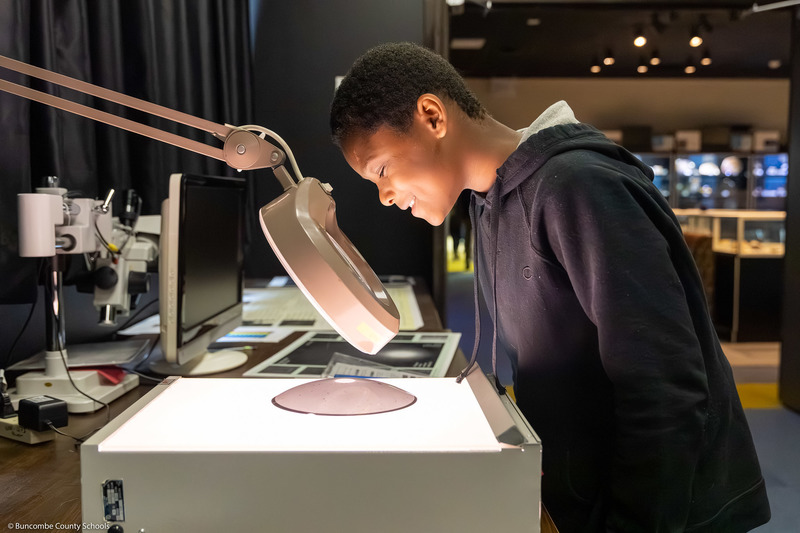 A student looks through a large magnifying glass.