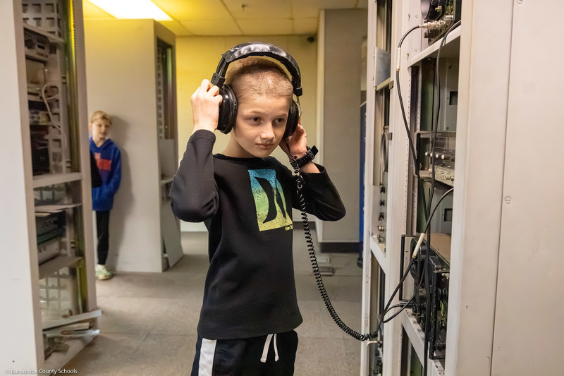 A student puts headphones on and stands by vintage equipment.