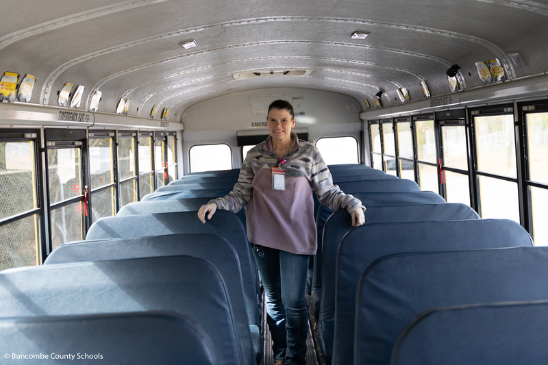 Lisa Rice standing in the isle of the school bus smiling at the camera. 