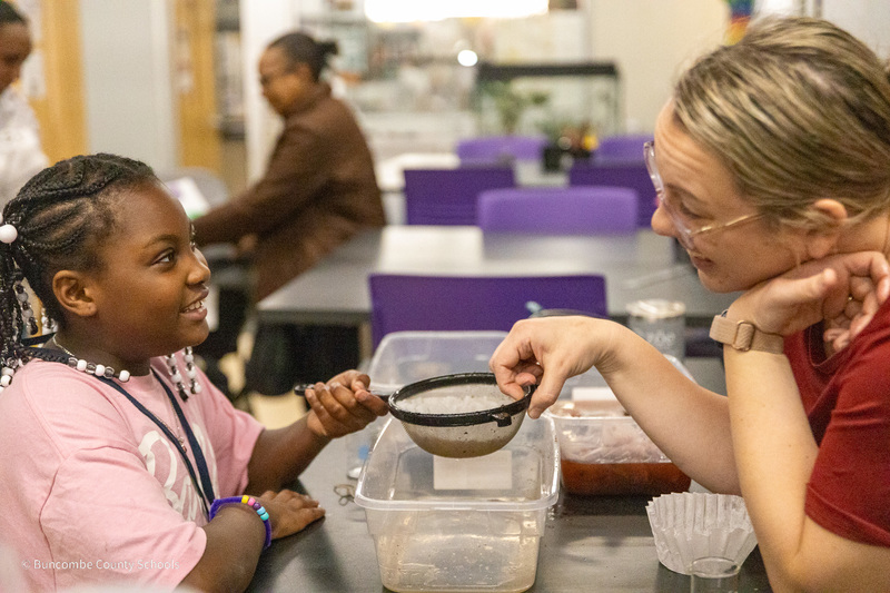A student faces a teacher holding a coffee filter as they perform an experiment