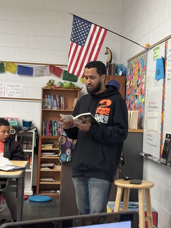 Isa Ibn Wali reading a passage from a book to students.