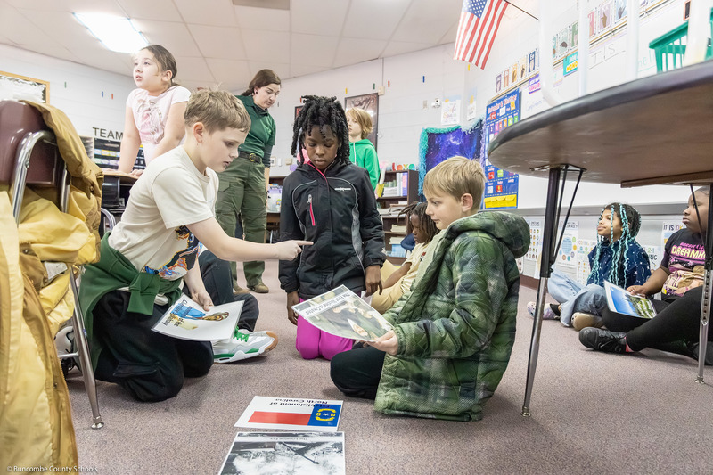 Students work together placing laminated sheets on the classroom floor.