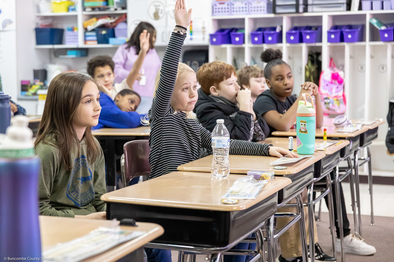 A student raises her hand among a row of desks.
