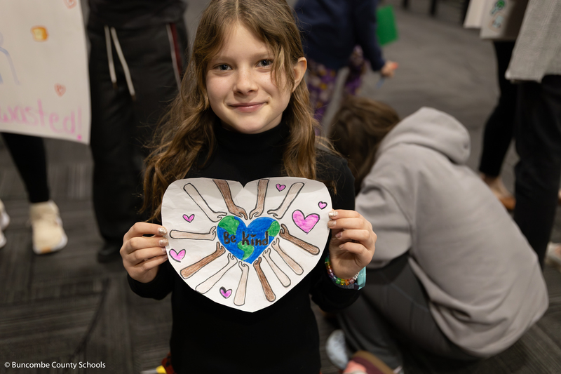 Student holding her artwork that says Be Kind.
