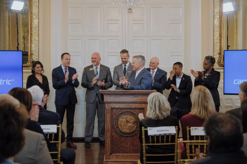 Gov. Stein stands behind a podium surrounded by industry and education leaders applauding.