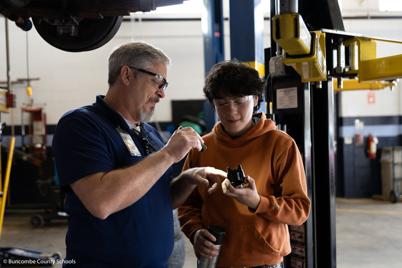 Mr. Clements showing a student a part to a vehicle. 