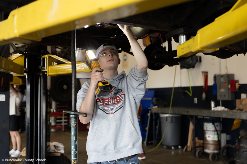 Student working on something underneath a vehicle. 