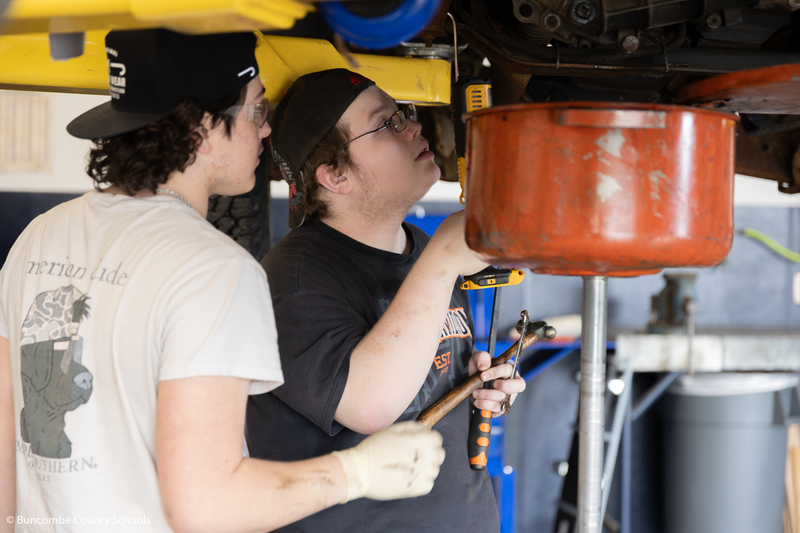 Students working on something underneath a vehicle. 
