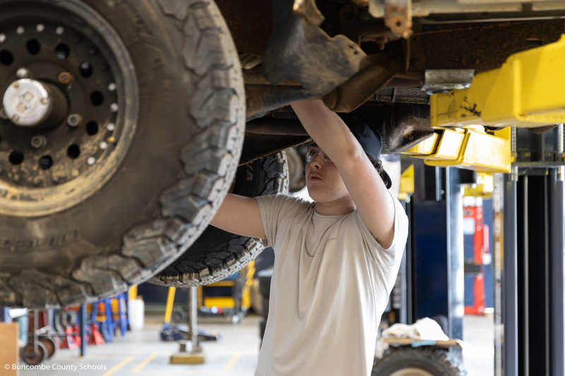 Student working on something underneath a vehicle. 