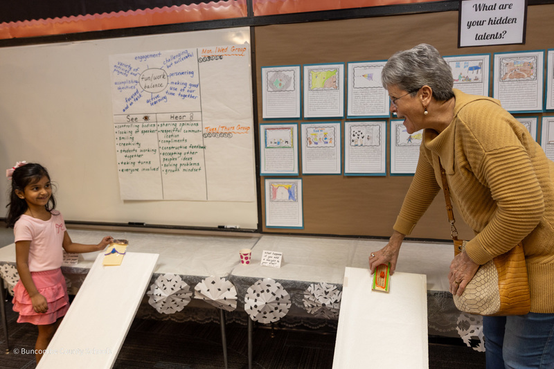 A student and her grandmother place toy sleds on ramps to race them.