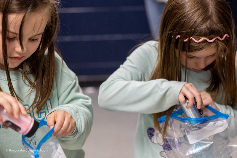 Two girls put glitter in sandwich bags to crete a snow globe.