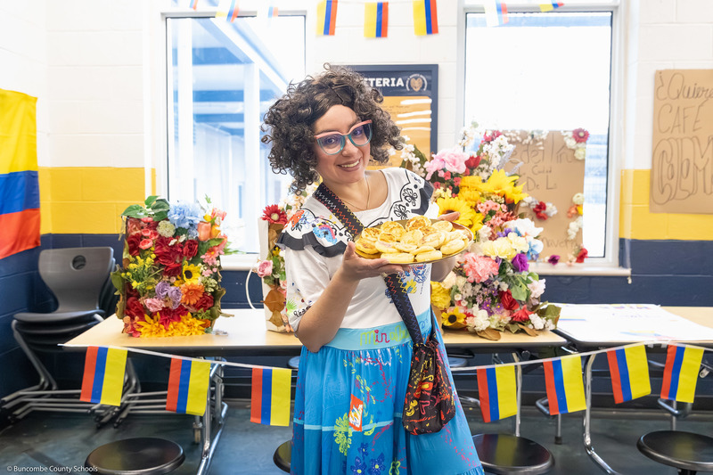 An adult in cultural attire smiles while holding a plate of food.
