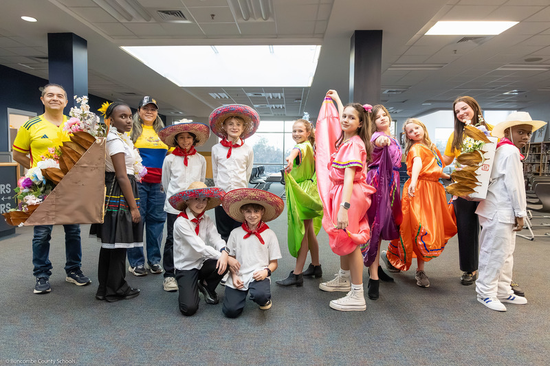 A group of adults and kids in cultural dress pose in Koontz's media center.