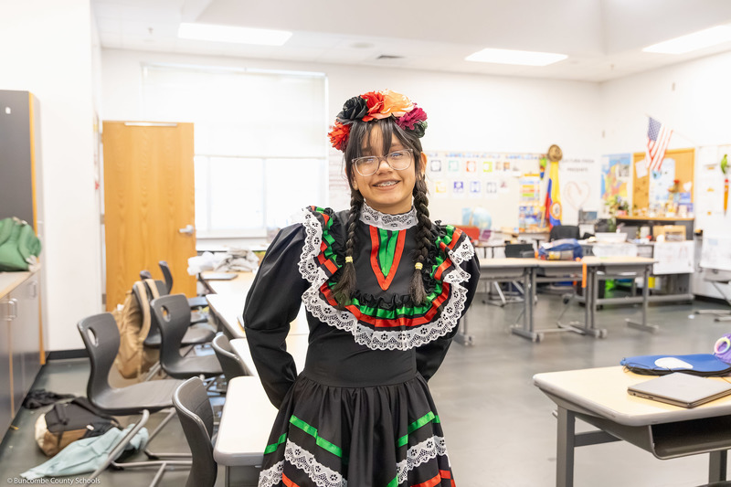 A student in cultural attire poses in a classroom.