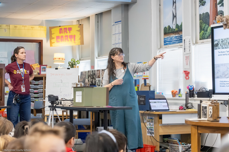 One of the two visitors shows examples of crankie boxes on a digital projection screen.