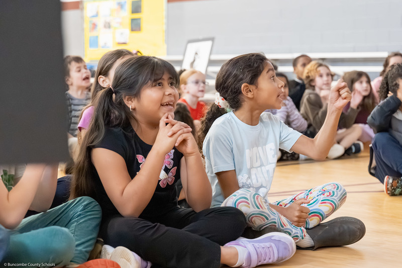 Students smile while listening as Susie Gardner reads her book.