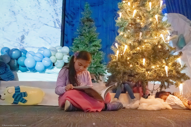 A student reads a book next to a lit Christmas tree.