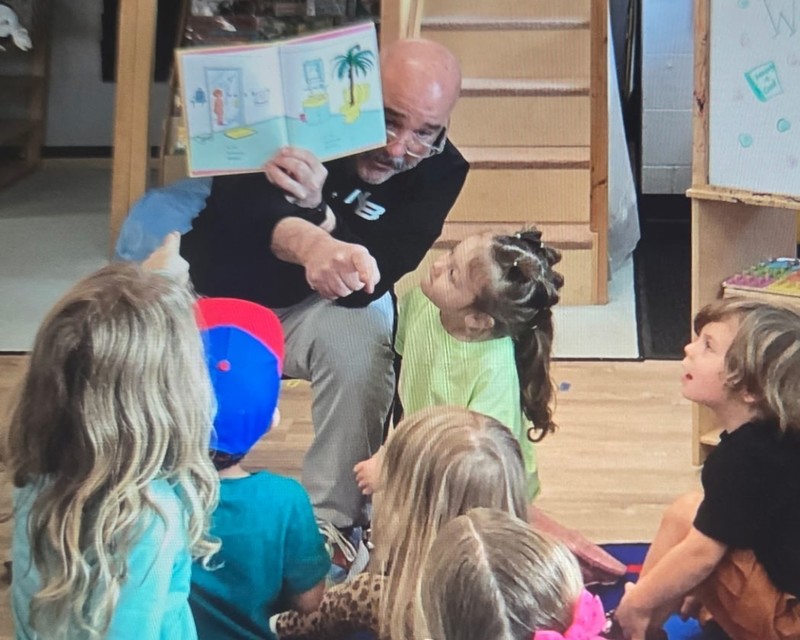 A principal holds up a book while students look at the picture.
