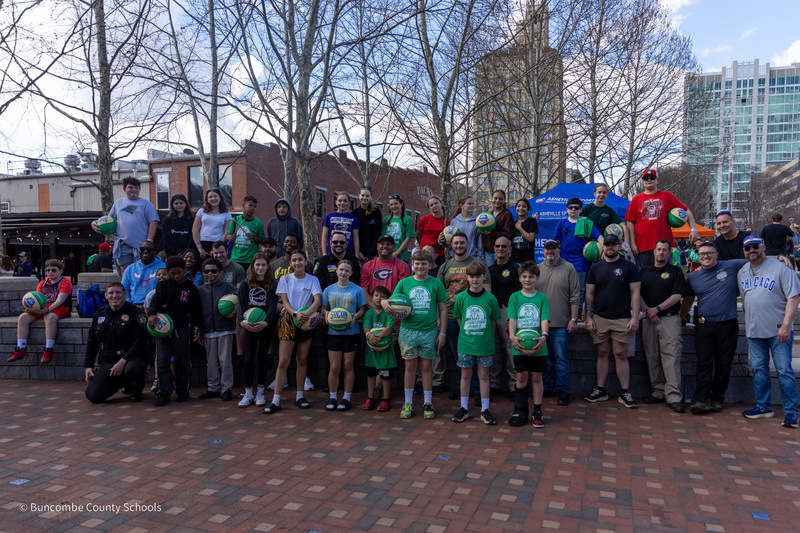 A group of school resource officers and students pose in Pack Square Park. The students are holding basketballs.